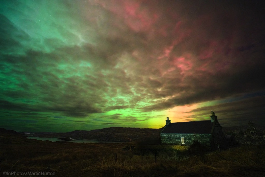 Northern lights over a crofting landscape against the cloudy sky in the Outer Hebrides